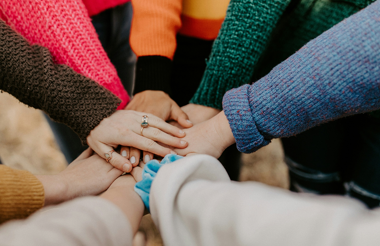 A top-down view of a group of people stacking their hands together in the center, symbolizing community.